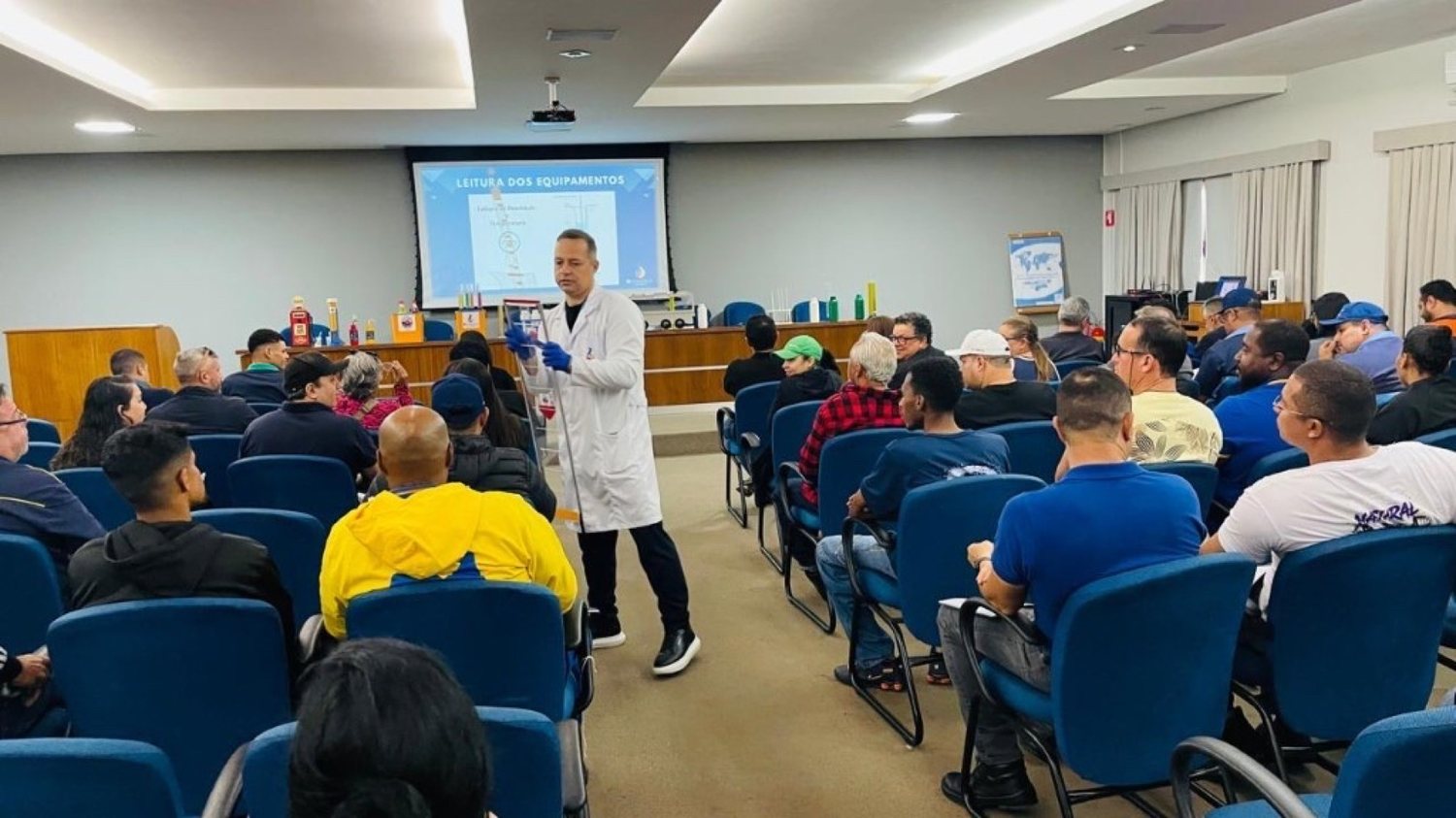 Instrutor da IC Analítica conduz demonstração prática entre a turma, com leitura de equipamentos ao fundo
